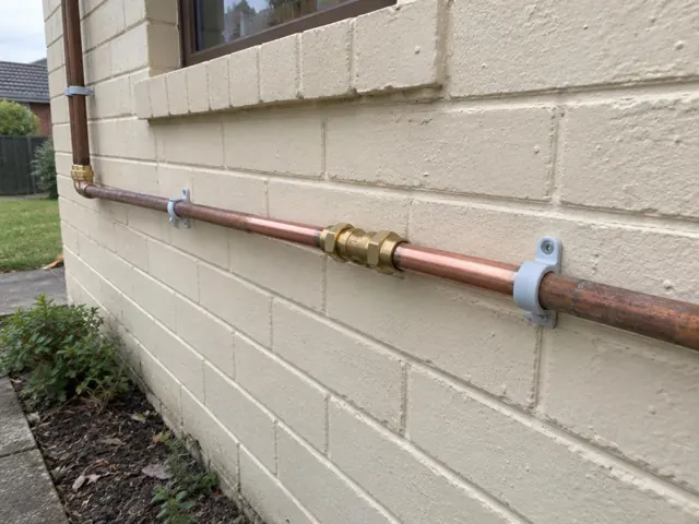 Repaired copper water pipe on an exterior brick wall beside a window in Gateshead