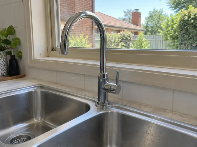 Chrome kitchen mixer tap beside a double stainless sink under a window in a tiled home kitchen in Dudley