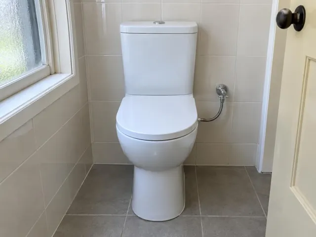 White toilet in a tiled bathroom beside a frosted window and door in Dudley